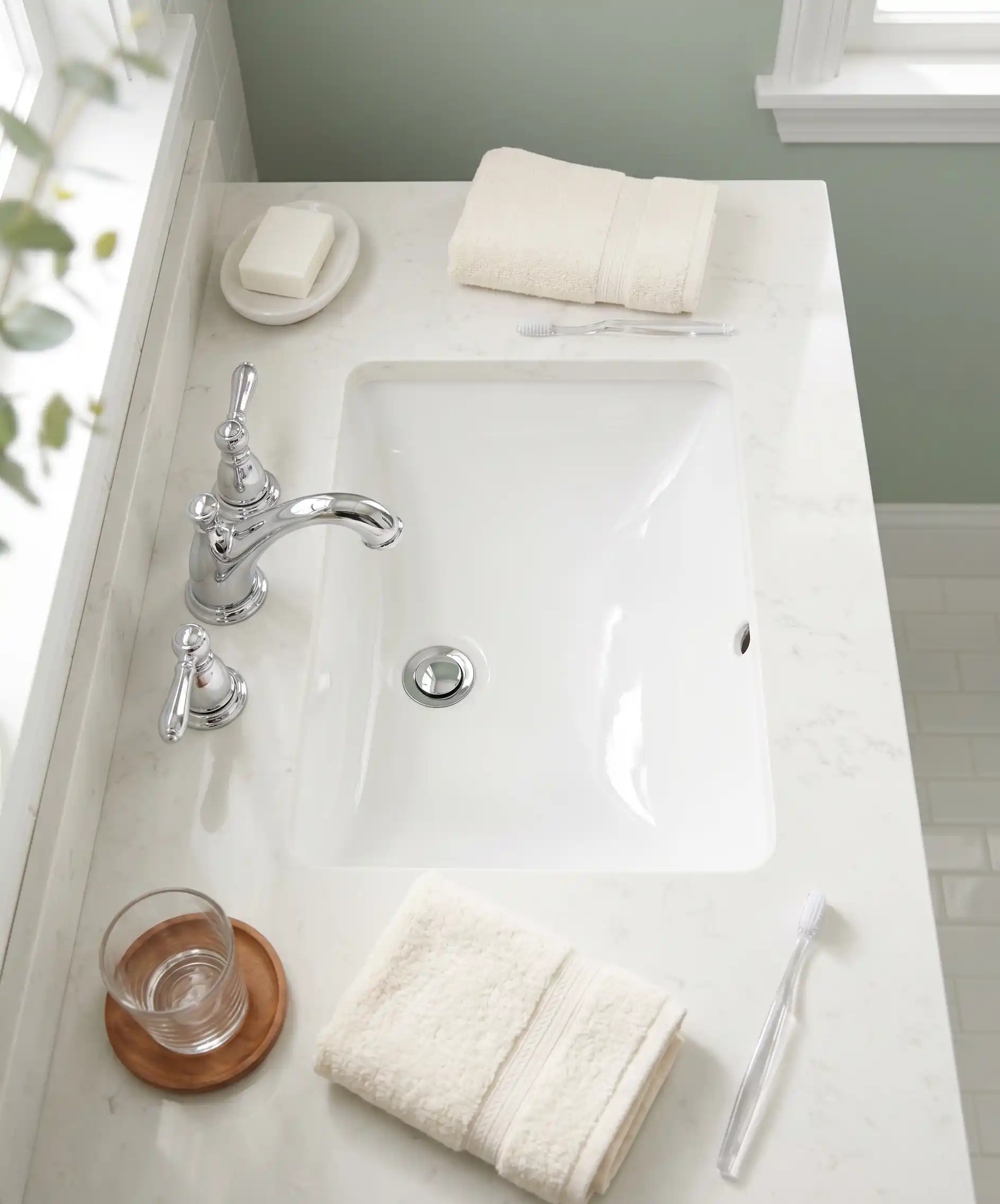 A bright, clean bathroom sink photo from above &mdash; gleaming white porcelain, clean faucet handles, a neatly folded hand towel to the side, no toothpaste residue or water spots &mdash; the 30-second wipe result.